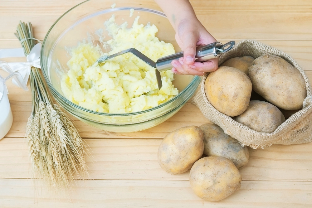 A potato masher being used to mash the softened potato chips