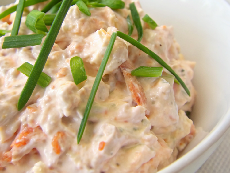 Ultra-close-up view of smoked salmon spread elegantly plated with a side of crackers and sliced cucumbers. The presentation is clean and inviting, highlighting the creamy texture and flecks of herbs.