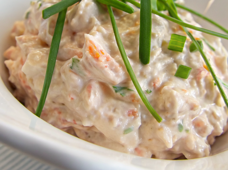 Ultra-close-up, high-quality image of a single serving of smoked salmon spread, capturing its creamy texture with flecks of fresh herbs and rich, flaked salmon. The spread is elegantly presented in a small dish with a slight swirl on top, garnished with a sprig of dill. The background is softly blurred, focusing entirely on the dip’s luscious consistency and delicate details.