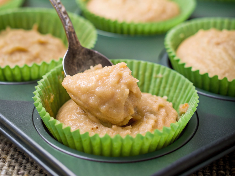 Ultra-close-up view of a spoon scooping thick muffin batter into paper-lined muffin cups, with a smooth and even distribution.